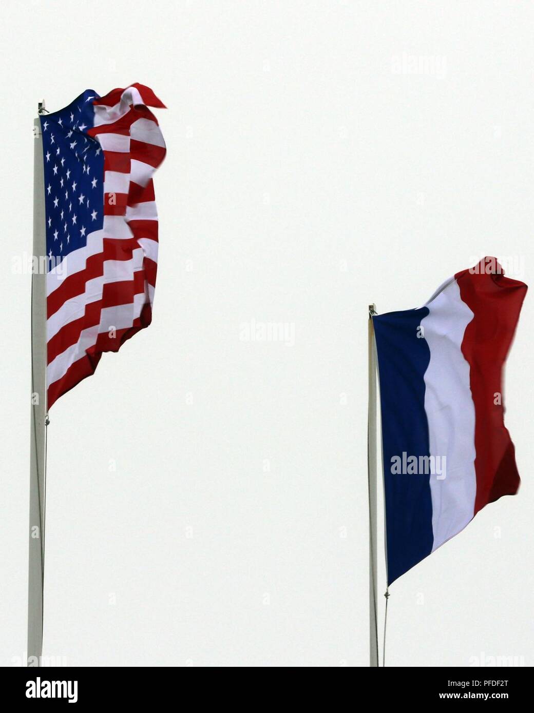 Flags of the United States of America (left) and France (center) wave in the wind during the 74th D-Day commemoration ceremony June 6, 2018 at Utah Beach along the coast of France. These flags fly together as a testament to their partnership and dedication to one another while recognizing the sacrifices of each country during WWII. Stock Photo