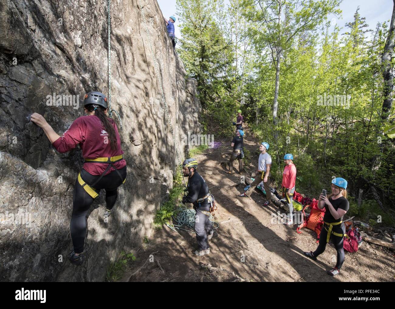 A group of climbers look on and cheer as two climbers in their group ascend during an Outdoor Adventure Program rock-climbing trip at Pivot Point Trail near Anchorage, Alaska, May 31, 2018. The OAP offers low-cost opportunities for the Joint Base Elmendorf-Richardson community to explore Alaska while also supporting the development of mission-ready military families and members. Stock Photo