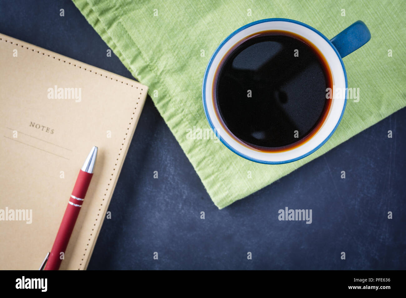Getting ready to write with a coffee and notebook with a green napkin on a black chalk surface. Stock Photo