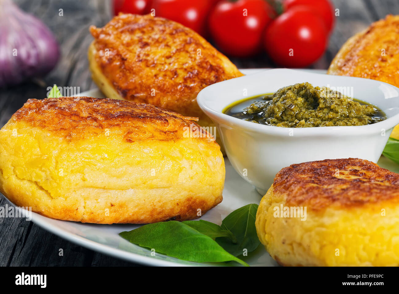 delicious Mashed Potato Pancakes with chicken Meat Filling on white dish with sauce pesto in gravy boat, fresh tomato on old wooden table, close-up Stock Photo