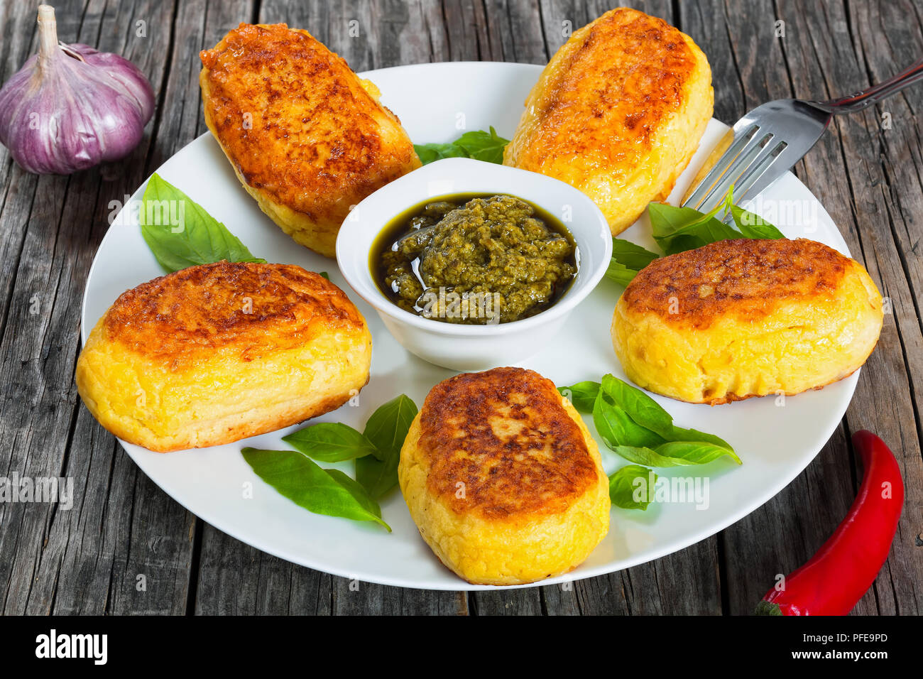 delicious Mashed Potato Pancakes with ground chicken Meat Filling on white dish with sauce pesto in gravy boat, fresh tomato on old wooden table, clos Stock Photo