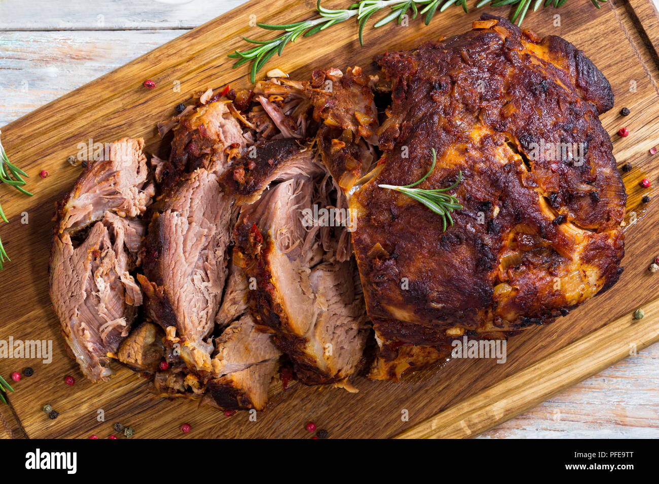 Roasted Pork shoulder cut on slices on chopping board with rosemary and