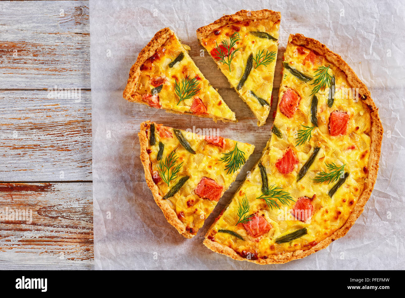 delicious homemade french quiche with red fish, green bean, sauce bechamel and Emmental cheese cut in slices on baking paper on white wooden backgroun Stock Photo