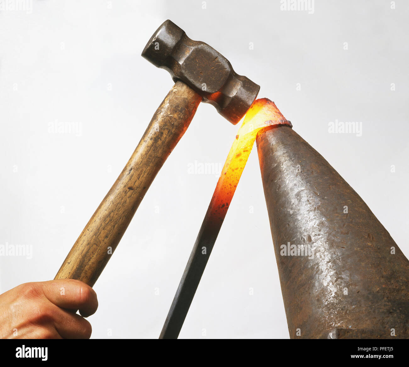 Red-hot steel bar being fashioned with a hammer, side view. Stock Photo