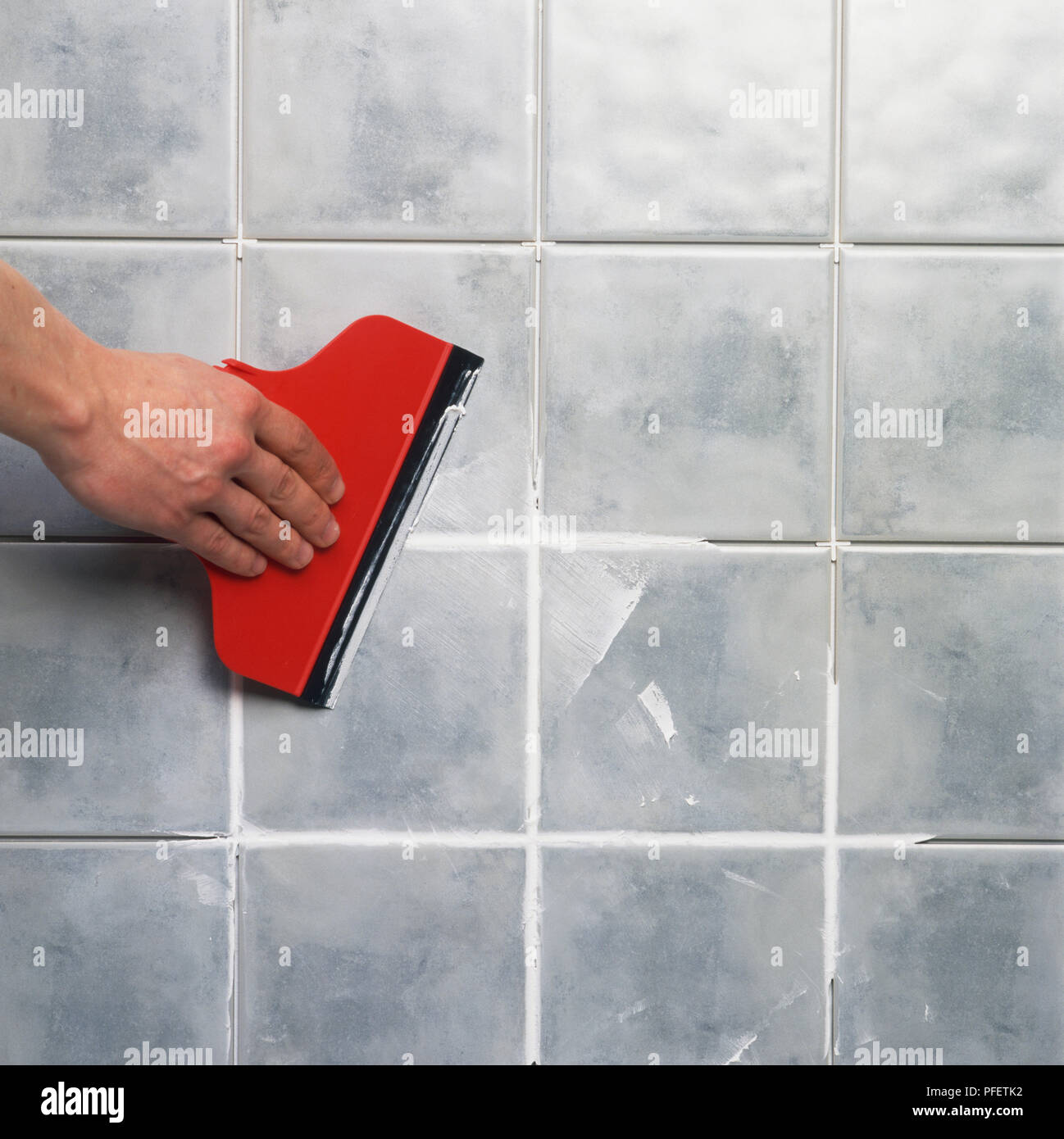 Grout being applied to tiles using a squeegee. Stock Photo