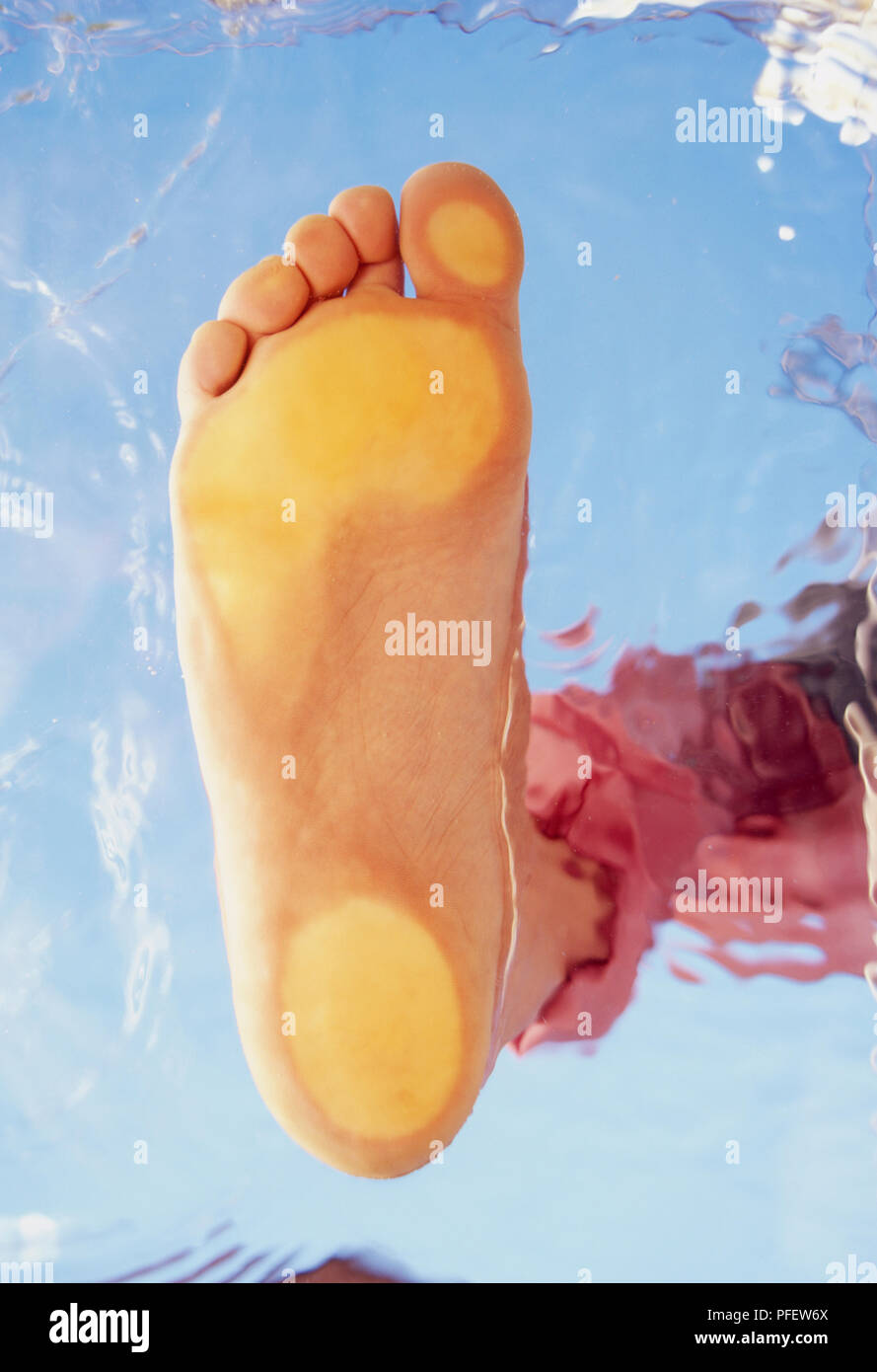 Sole of foot pressed on glass with water reflected in background, view