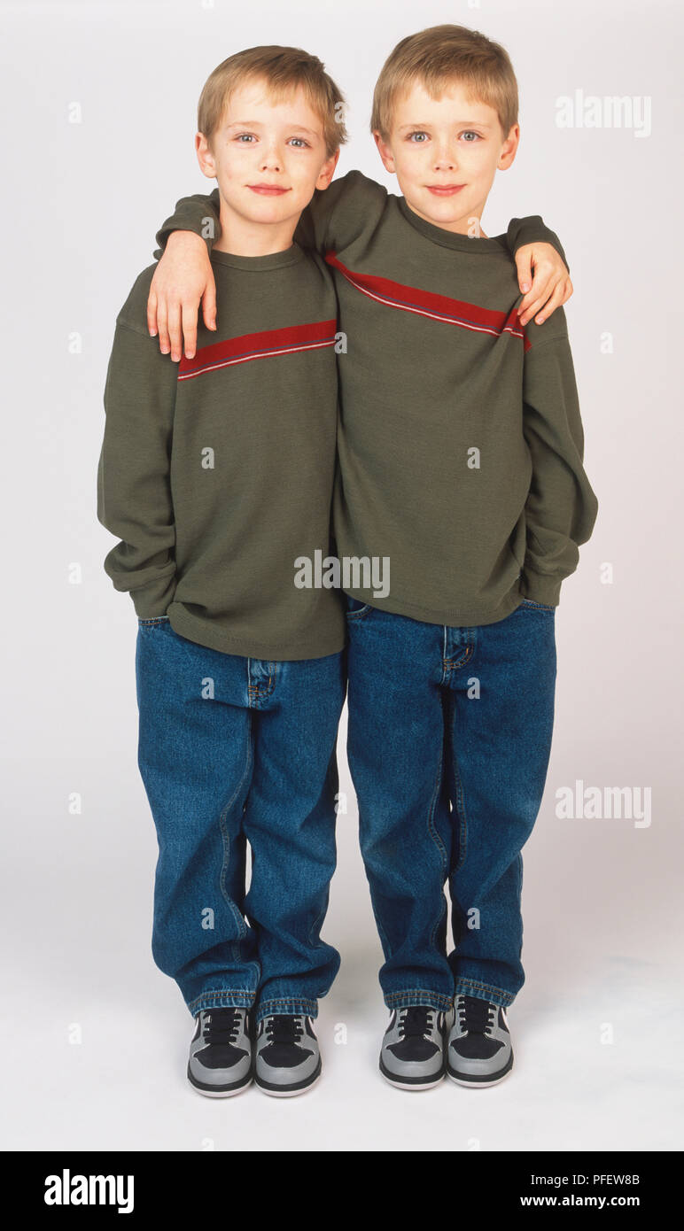 Identical twin boys with blonde hair and blue eyes standing with arm around each other's