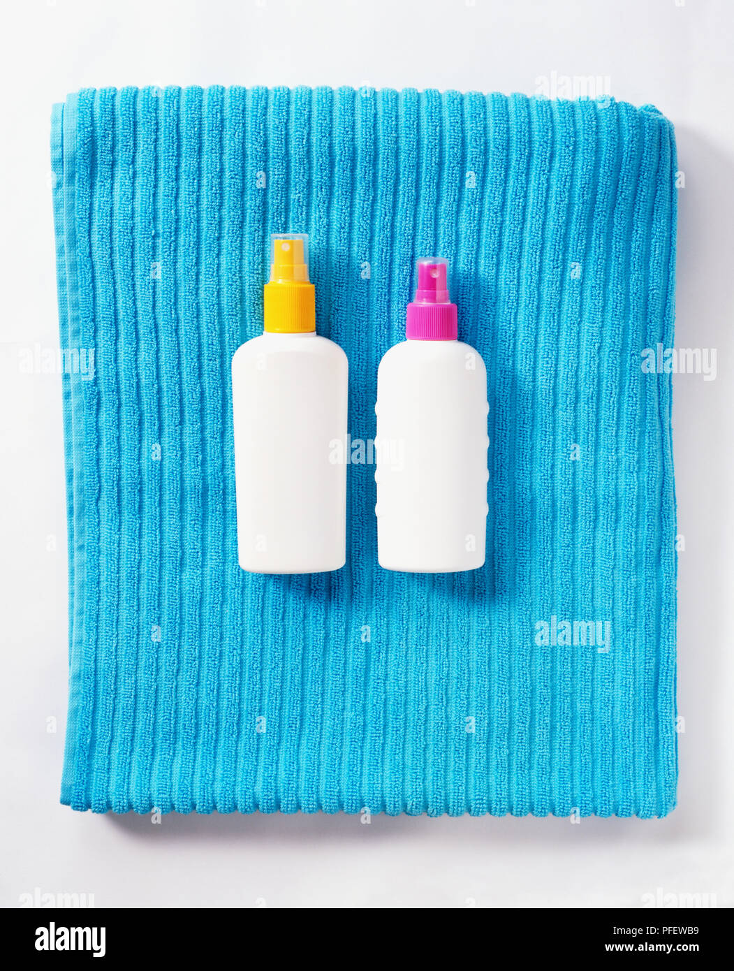 Two white plastic bottles with coloured lids lying on folded ribbed bath towel. Stock Photo