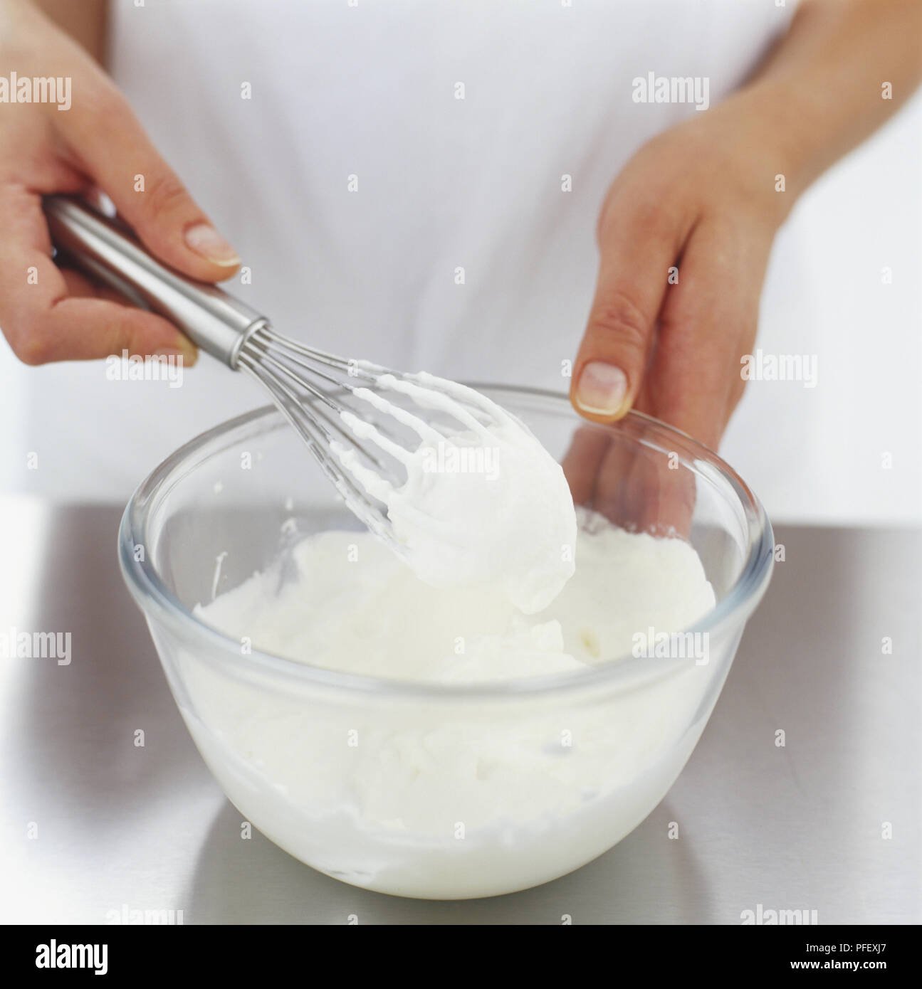 Metal whisk being used to whip cream in glass bowl, side view Stock
