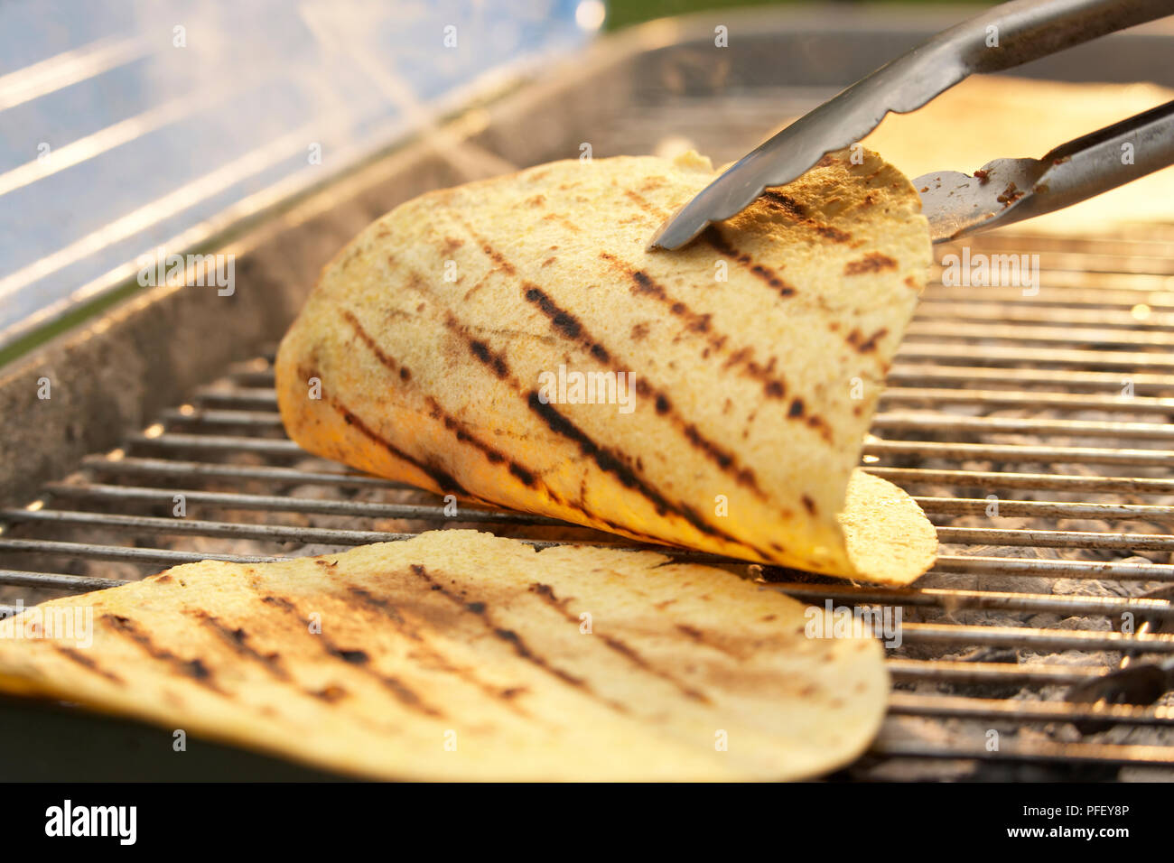 Tortillas on barbecue grill, being turned with tongs Stock Photo Alamy