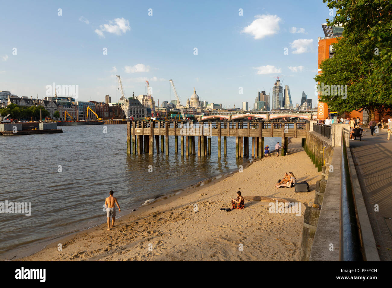 LONDON, UK - AUGUST 6, 2018 : People on the small beach at the shore of the Thames by Gabriel's Wharf on the South Bank of England's capital city with Stock Photo