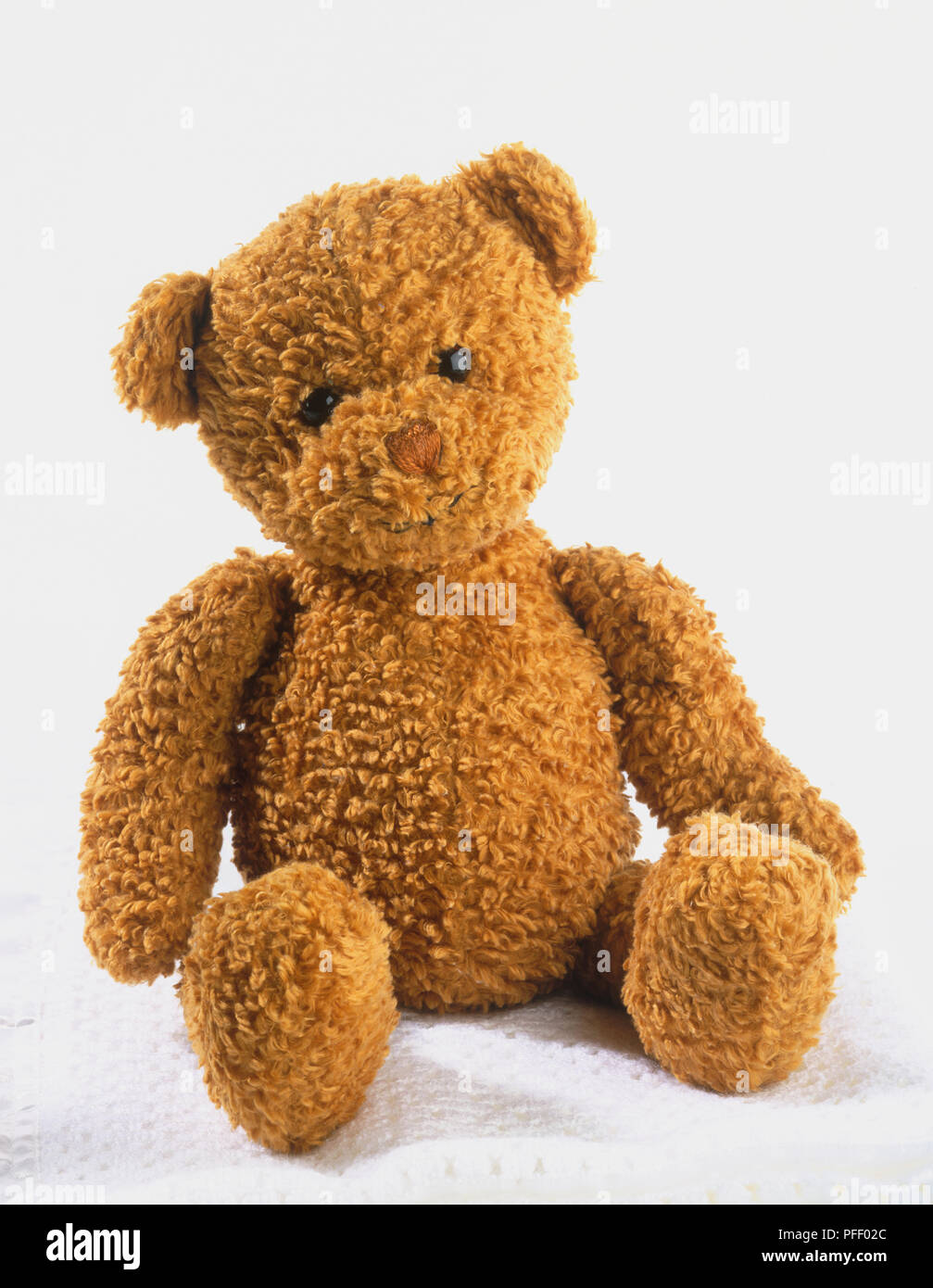 Brown teddy bear sitting on top of folded white blanket Stock Photo