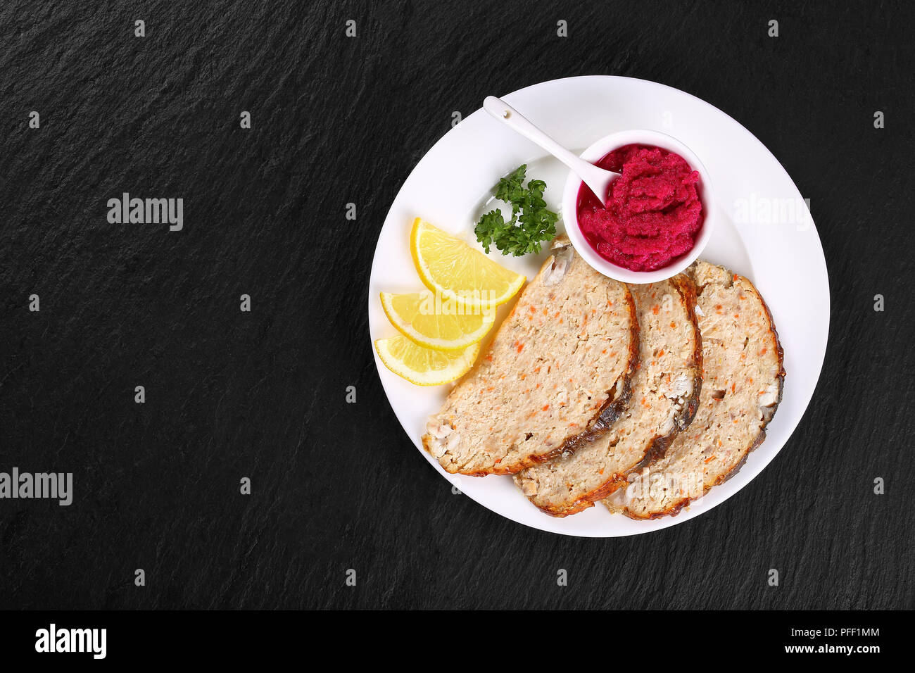 delicious baked in oven Gefilte minced carp fillets cut in slices with fresh parsley, lemon and horseradish beetroot sauce on white plate, on black sl Stock Photo