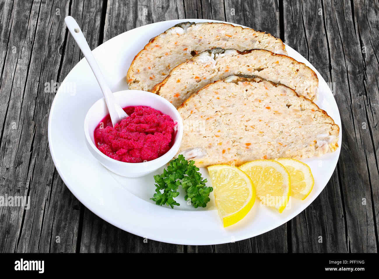 stuffed carp or minced-fish forcemeat stuffed inside the fish skin, cut in slices and served  with lemon slices and horseradish flavored with beetroot Stock Photo