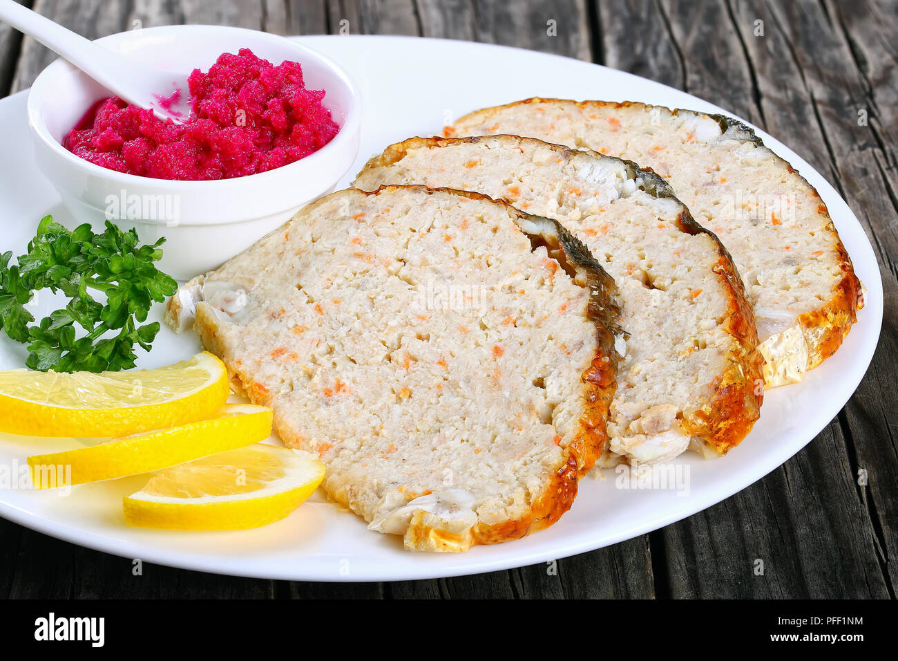 stuffed carp or minced-fish forcemeat stuffed inside the fish skin, cut in slices with lemon slices and horseradish flavored with beetroot on white pl Stock Photo