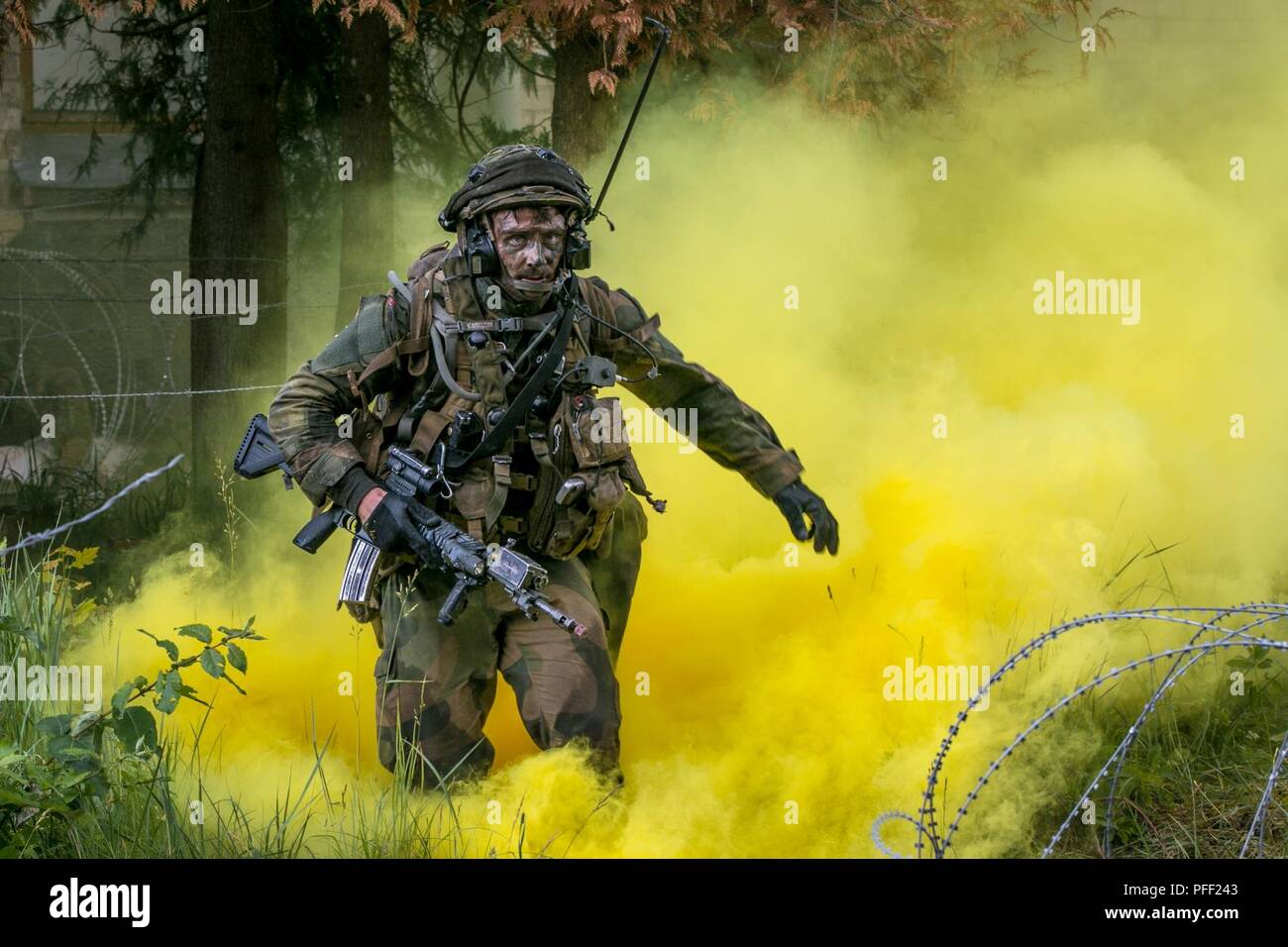 A Norwegian infantrymen assigned to Brigade Nord, Camp Skjold, Norway, bounds forward through dense yellow smoke while conducting military offensive urban training (MOUT) during Saber Strike 18 in Skrunda, Latvia, June 12, 2018. Saber Strike is a multinational exercise currently in its eighth year. This year's exercise, which is scheduled to run from June 3-15, tests participants from 19 countries on their ability to work together to promote stability in the region and improve each units ability to perform their designated missions. Stock Photo