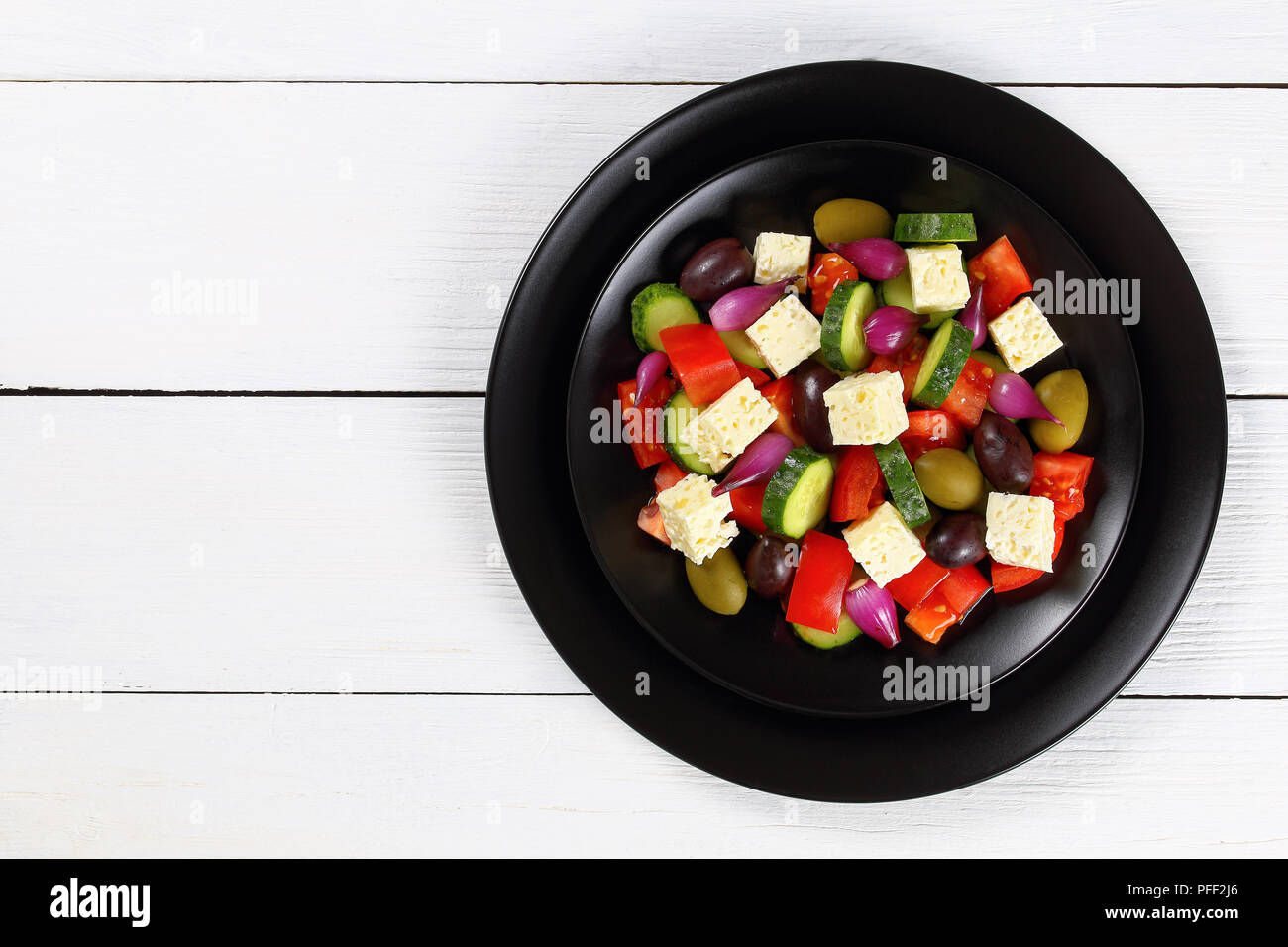 delicious Greek salad with fresh vegetables, feta cheese green and kalamata olives, red onion bulbs on black plates on white boards, view from above Stock Photo