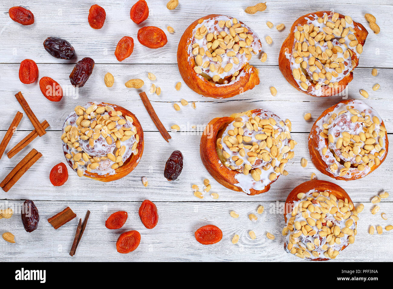 delicious freshly baked homemade cinnamon rolls topped with peanuts on wooden table with dried apricot, dried date fruits and cinnamon sticks, view fr Stock Photo