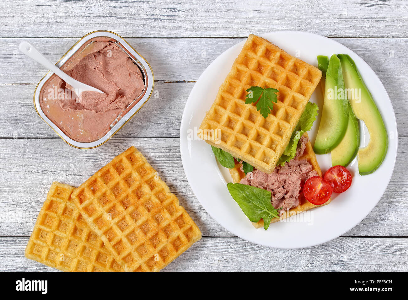 delicious salted belgian waffles sandwich with avocado slices, turkey liver pate, lettuce, spinach and parsley on white plate with cherry tomatoes, an Stock Photo