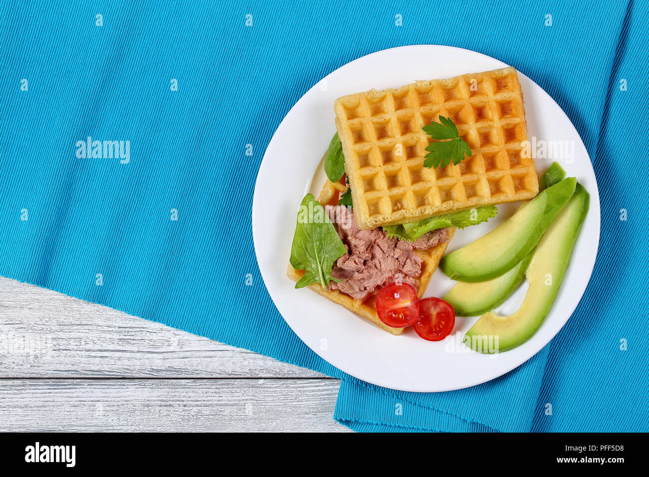 delicious salted belgian waffles sandwich with avocado slices, turkey liver pate, lettuce, spinach and parsley on white plate with cherry tomatoes, he Stock Photo