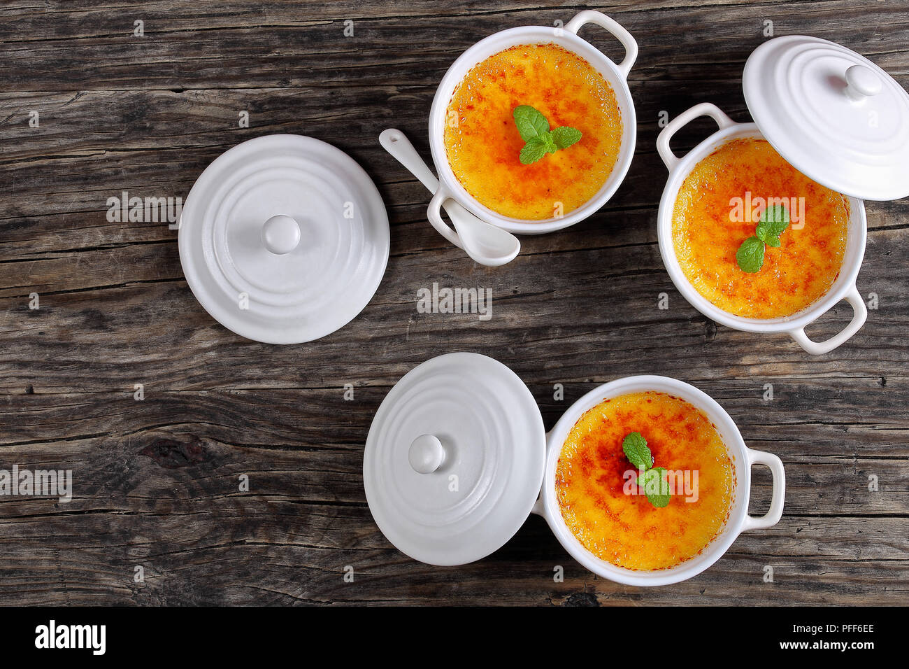 delicious Creme brulee - french dessert of custard with hard caramel top, decorated with mint leaves in white ceramic souffle dishes, authentic recipe Stock Photo