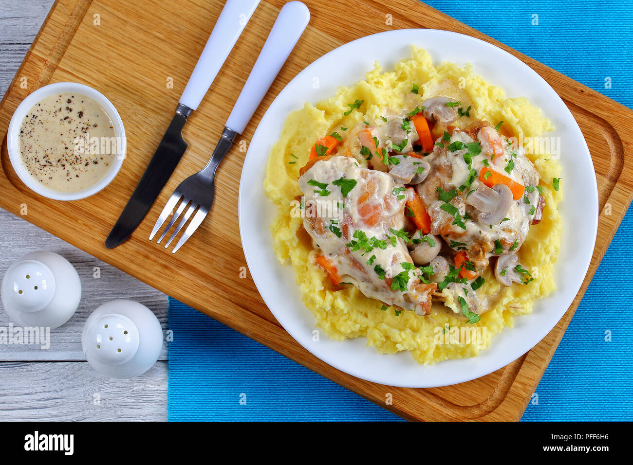 delicious Rabbit braised in sour cream with mushrooms and carrots served with mashed potatoes on white plate on wooden board with fork and knife, view Stock Photo