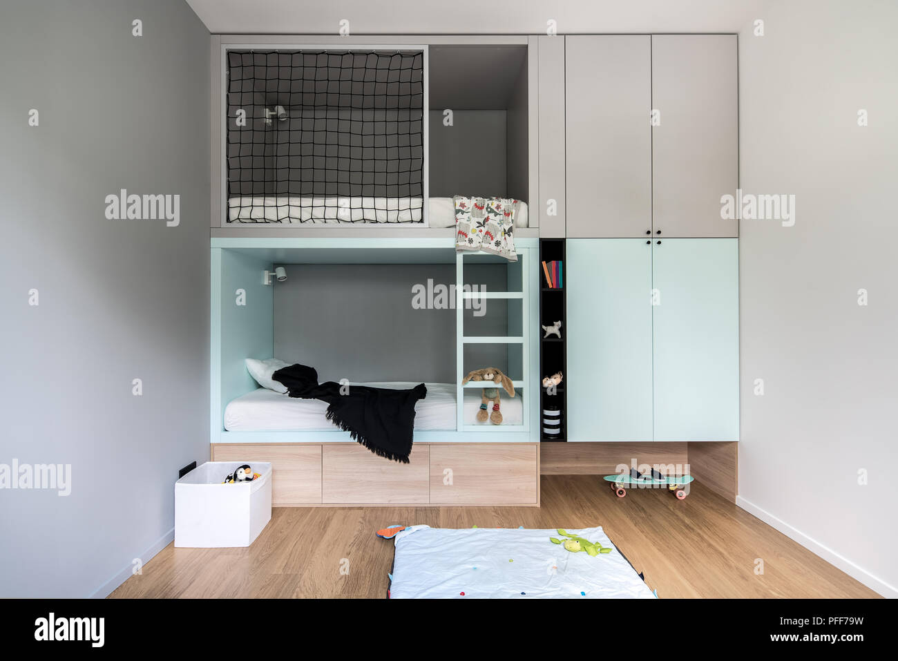 Kid's room in modern style with light walls and a parquet on the floor. There is a multicolored loft bed with lockers and shelves with toys and books, Stock Photo