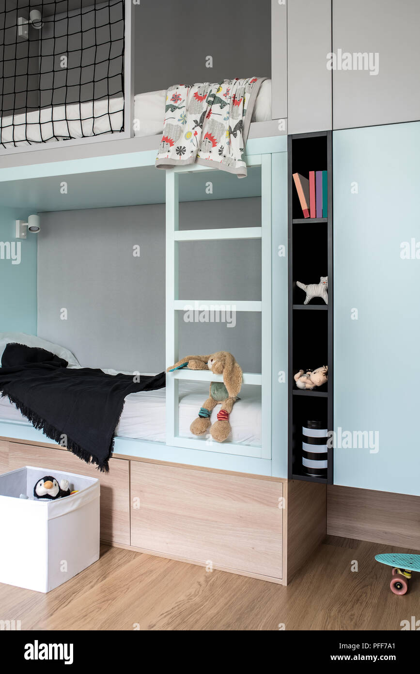 Nice kid's room in modern style with multicolored walls and a parquet on the floor. There is a cyan-gray loft bed with lockers and shelves with toys a Stock Photo