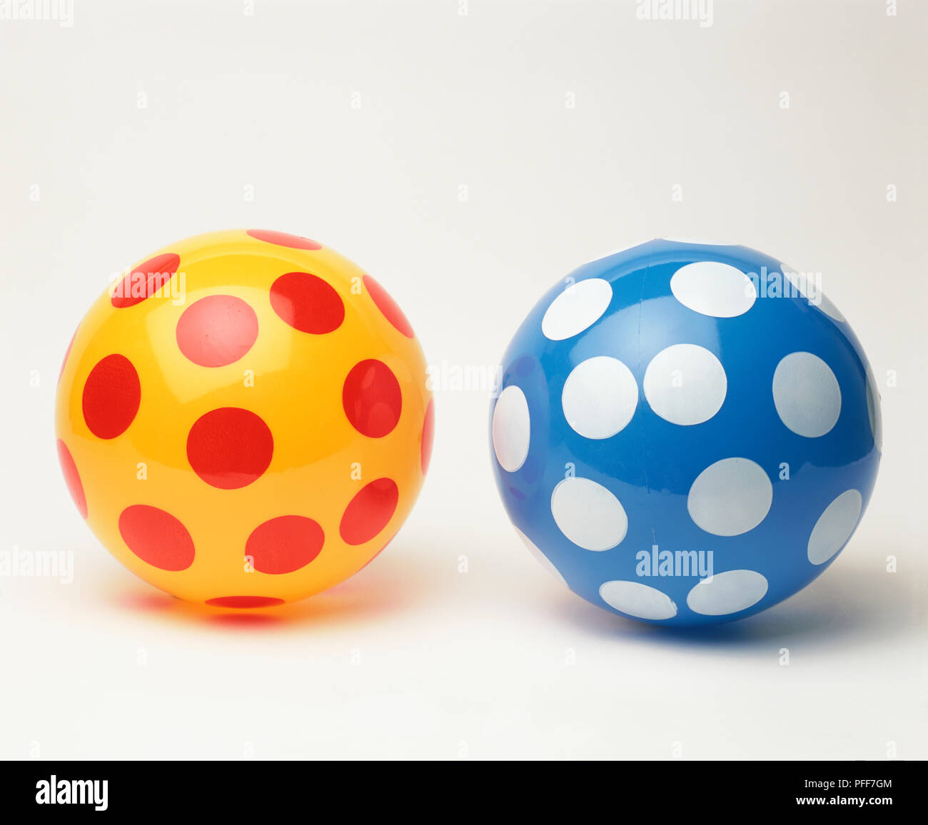 Yellow plastic toy ball with red polka dots, next to blue plastic ball with white polka dots. Stock Photo