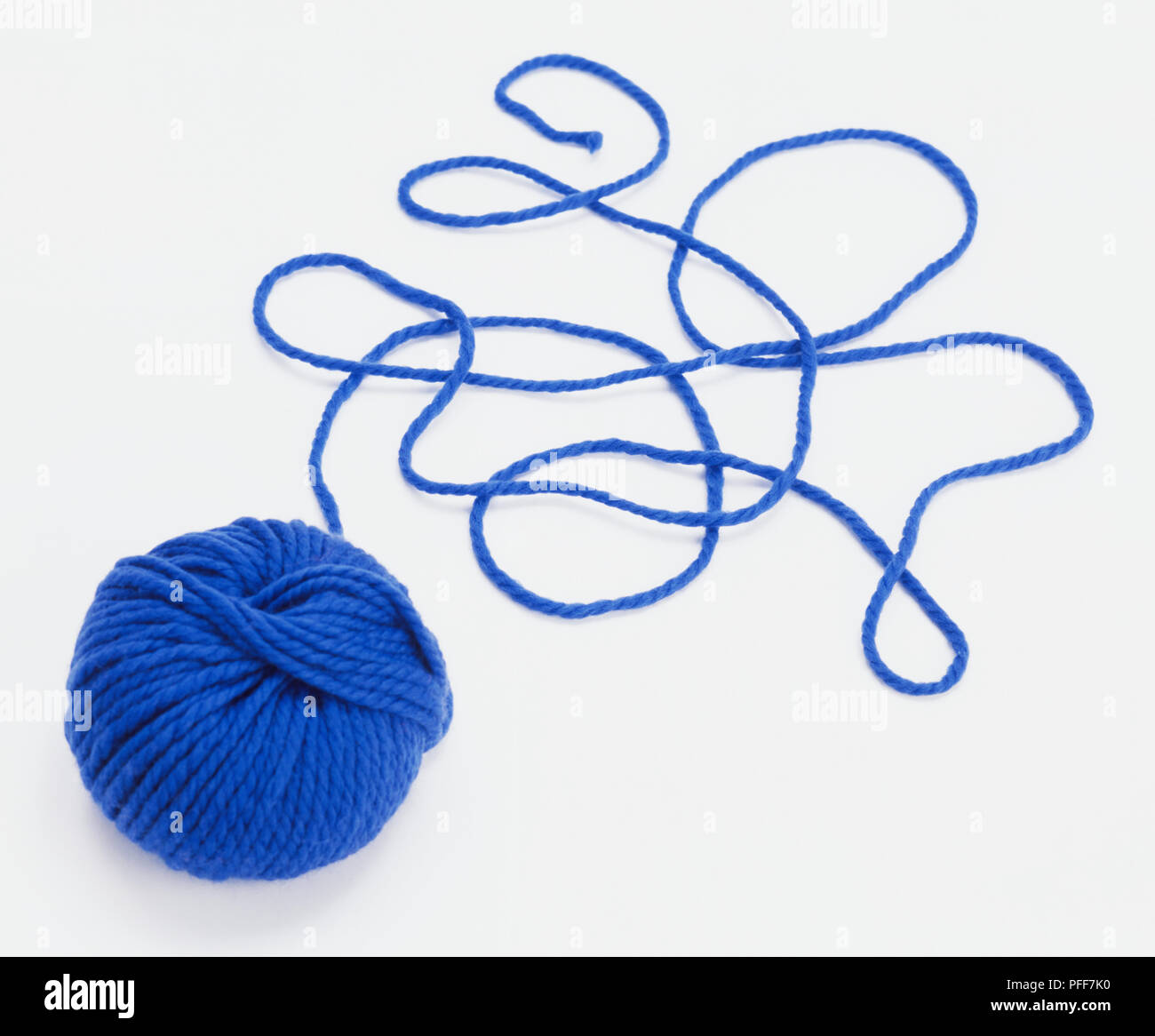 Ball of blue wool, perfect round ball, unravelled piece lying in a tangle on ground. Stock Photo