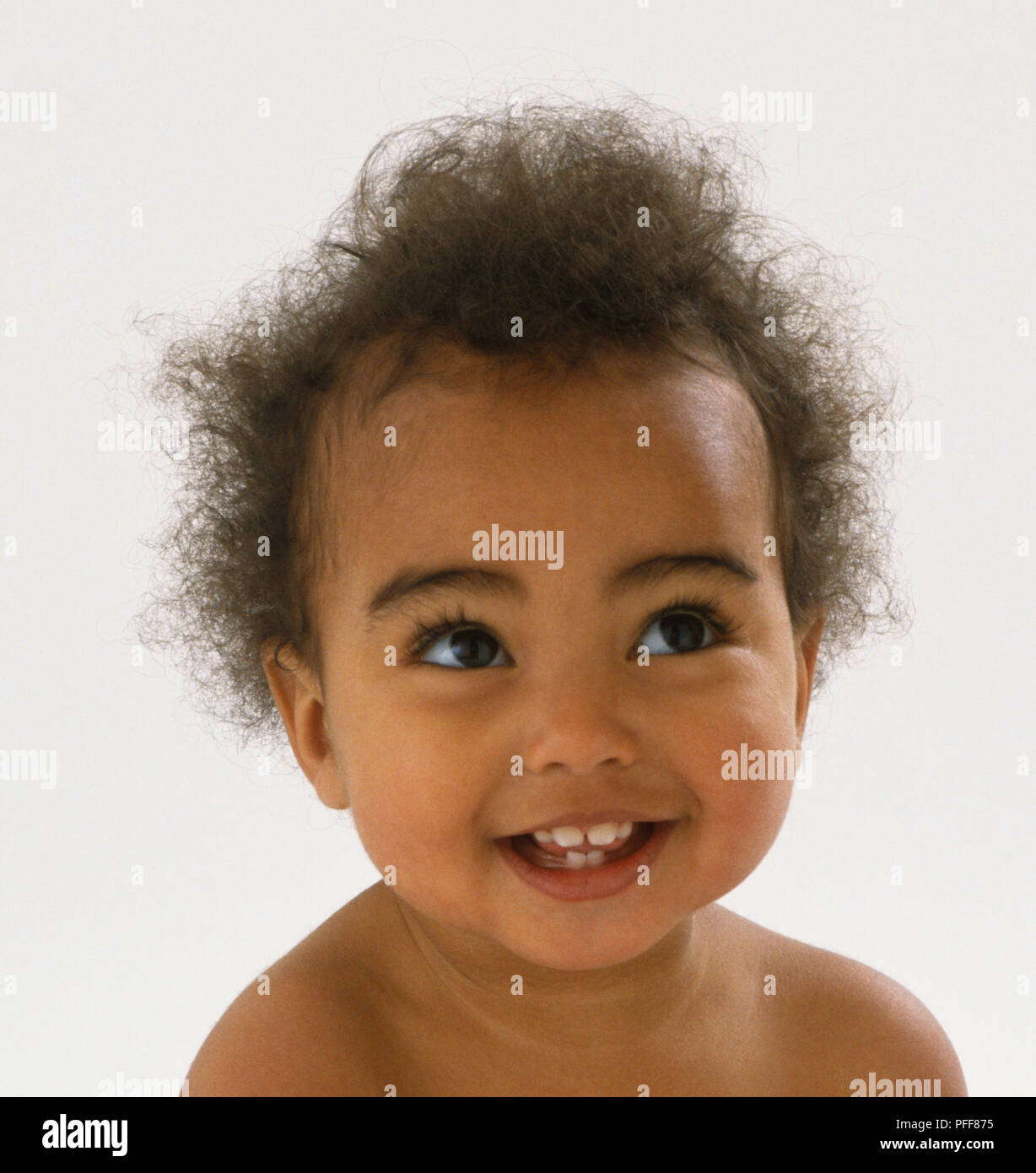 Baby with curly brown hair, defined eyebrows and brown eyes smiling