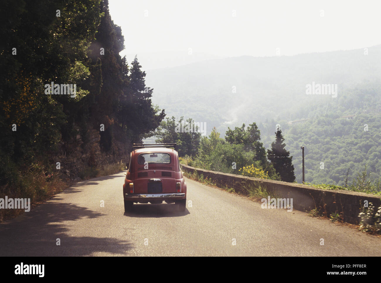 Italy, Eastern Tuscany, nr Borgo San Lorenzo, small red car travelling on mountain road, view from behind Stock Photo