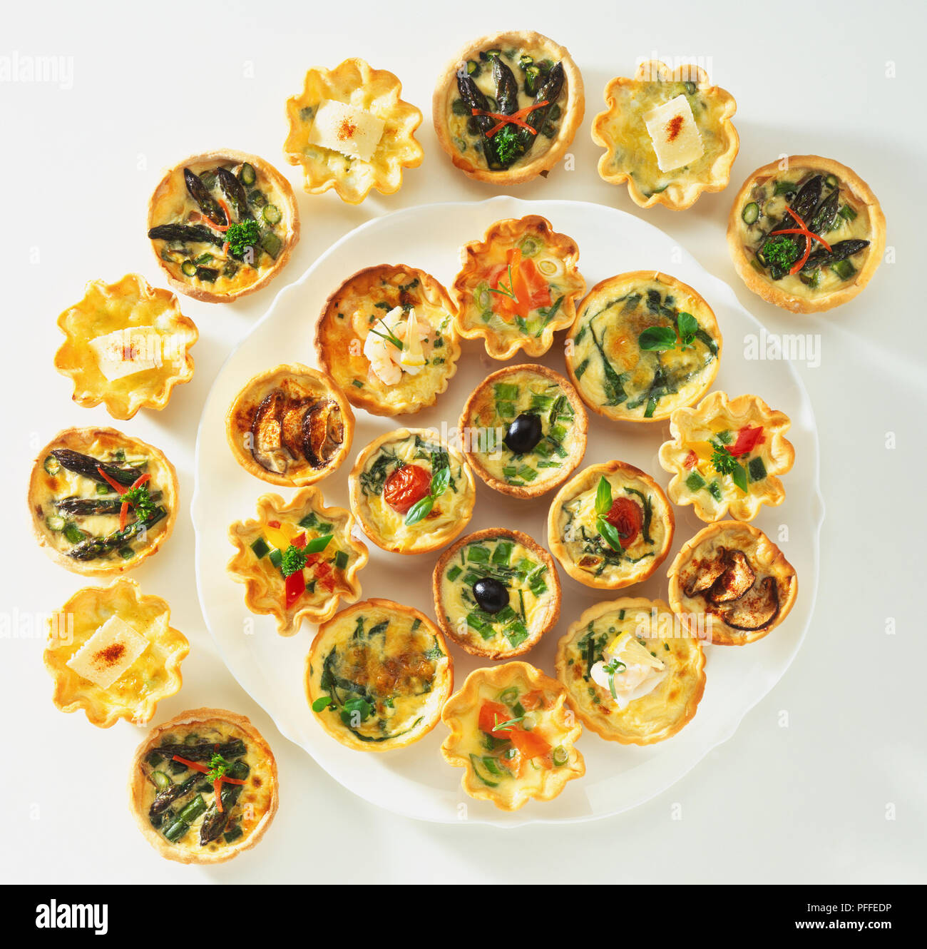 Various small quiches on a platter and in a semi-circle around it, view from above. Stock Photo