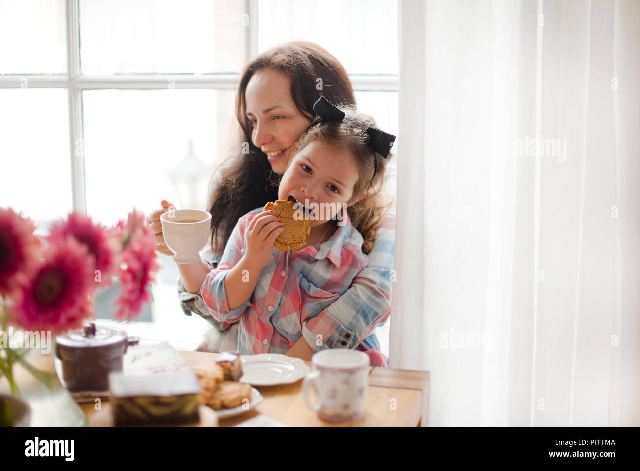 A woman and a little daughter are eating breakfast at home at a table by the window. Happy family and breakfast. Good morning at home. Free space for text. Stock Photo