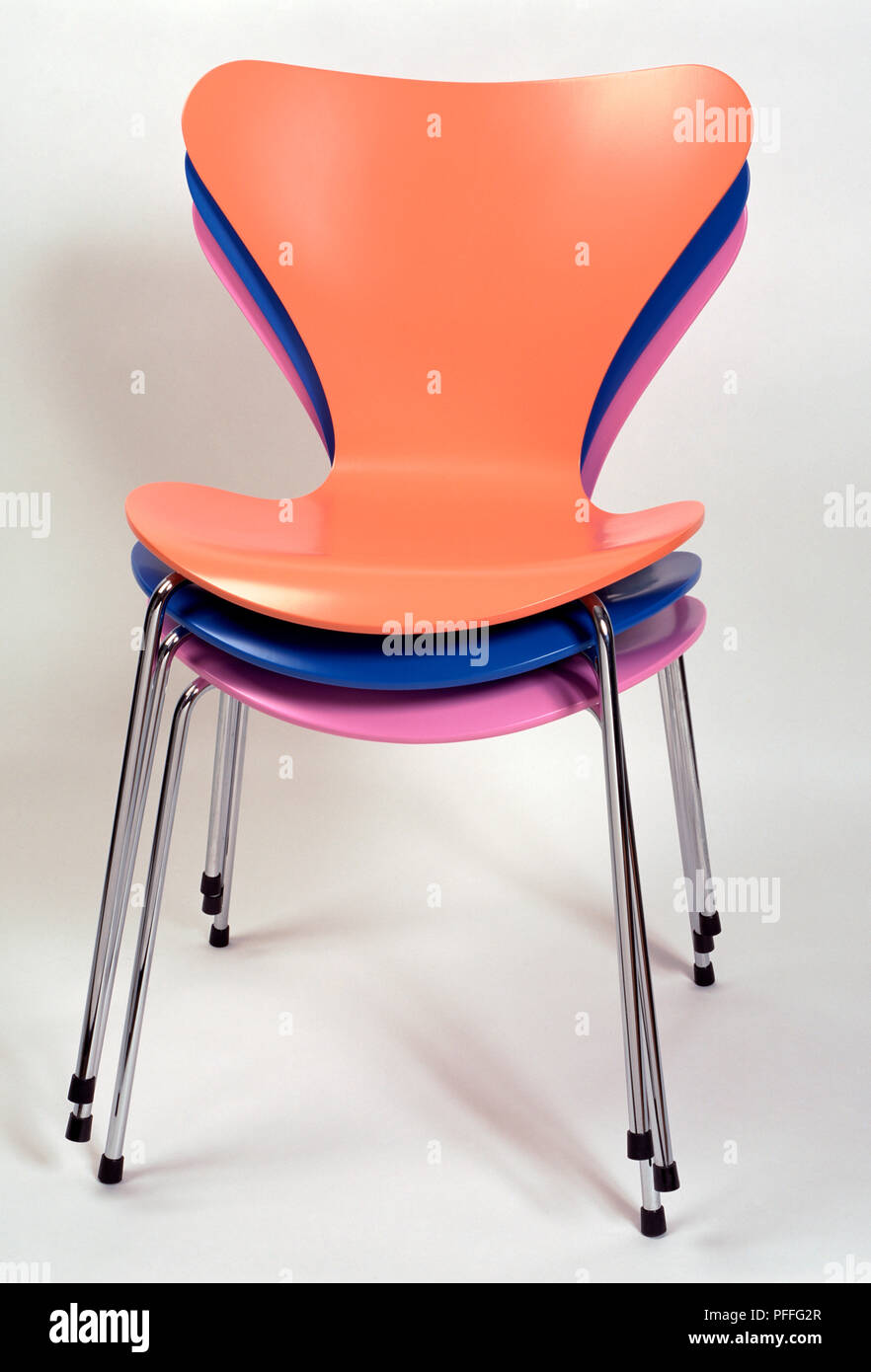 Three brightly-coloured plastic chairs stacked on top of one another. Stock Photo