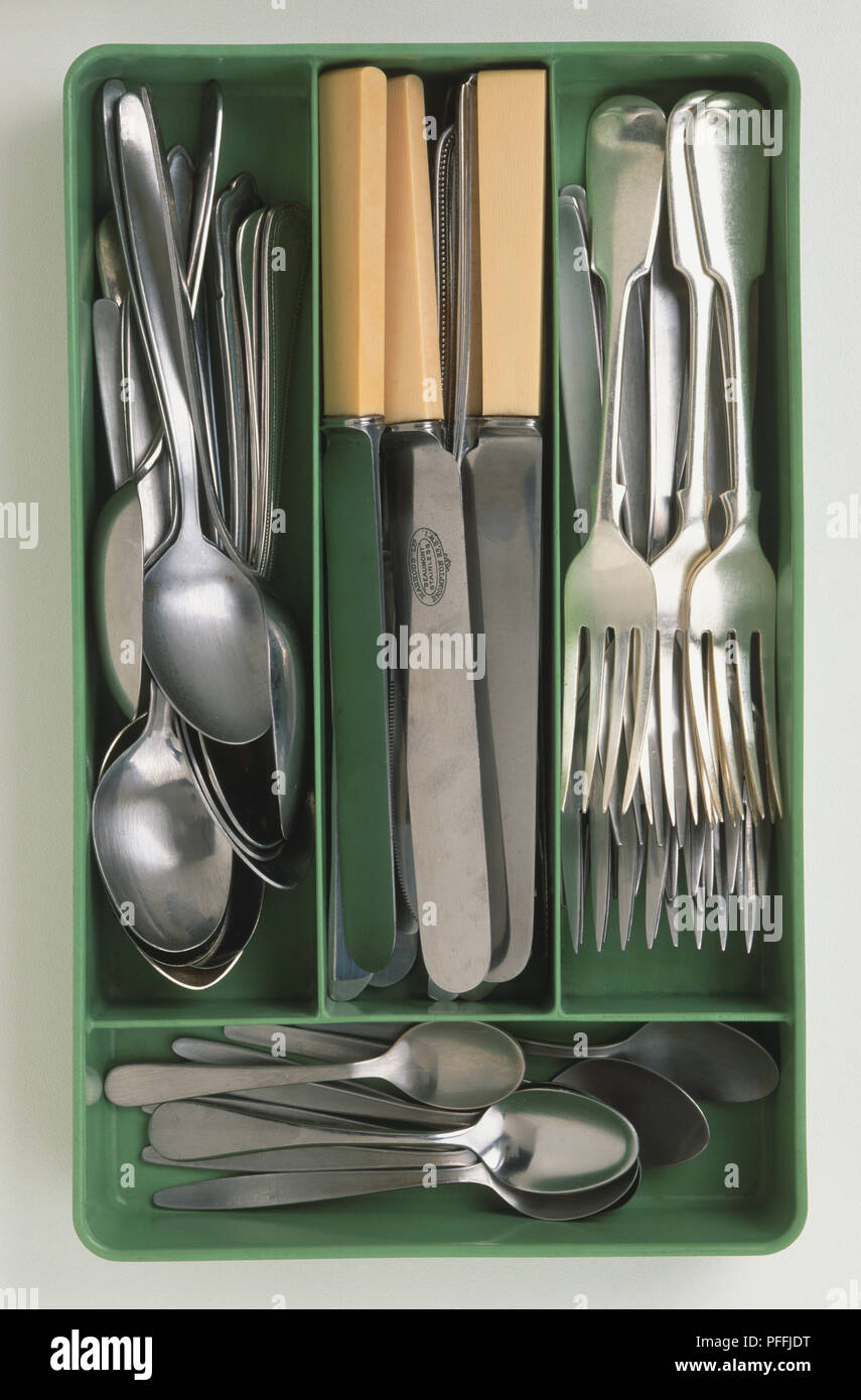 Pea-green coloured 1950s Bakelite cutlery tray, containing silver forks, spoons and bone-handled knives, above view. Stock Photo