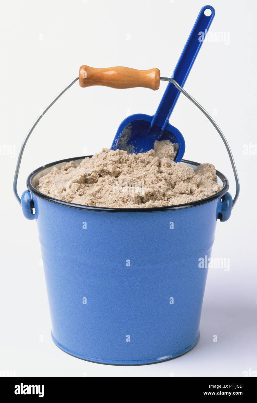 Child's pale blue metal bucket and spade with wet sand inside, front view. Stock Photo