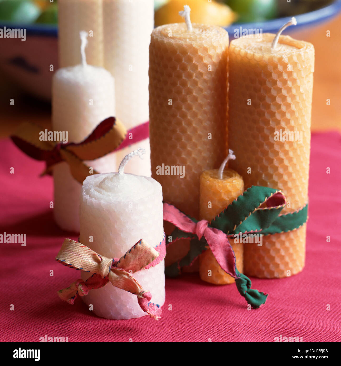 Assorted yellow and white rolled beeswax candles, honeycomb patterned surface, decorative ribbons tying candles together, new white wicks, standing on fuscia pink material. Stock Photo