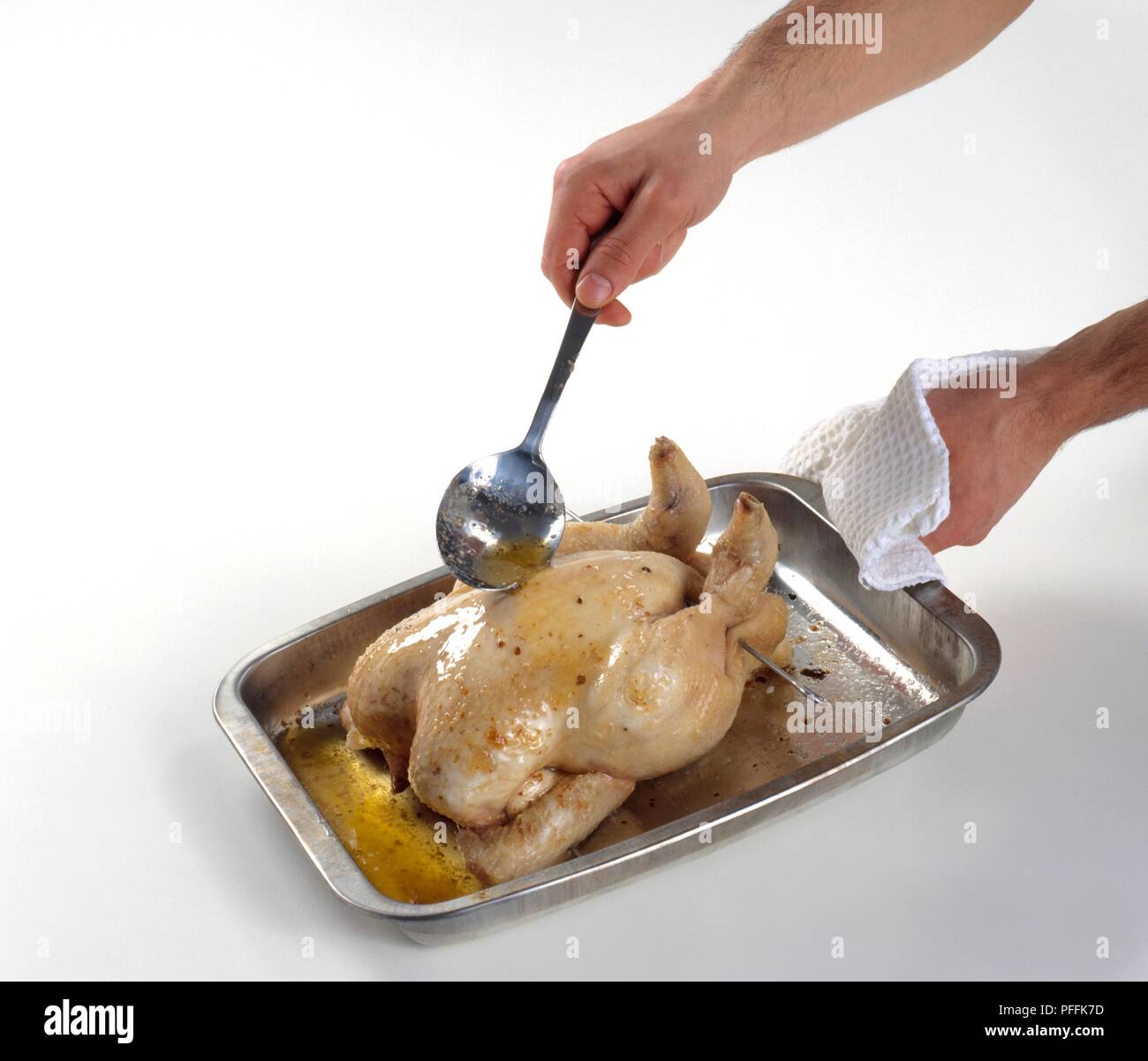 Chicken in roasting pan being basted with pan juice, using a spoon