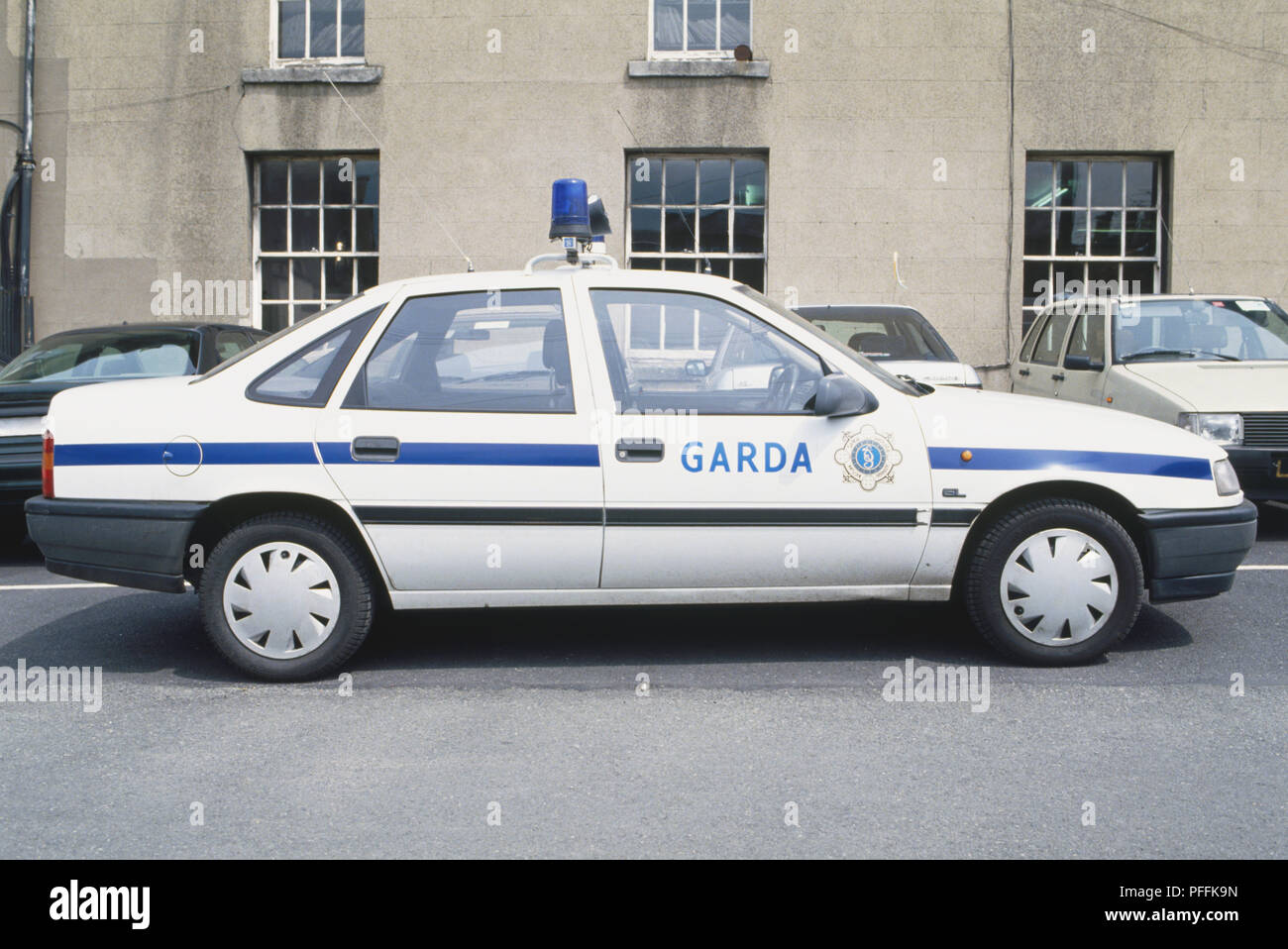 Republic of Ireland, Garda patrol car parked in front of civilian cars, outside grey building, side view. Stock Photo
