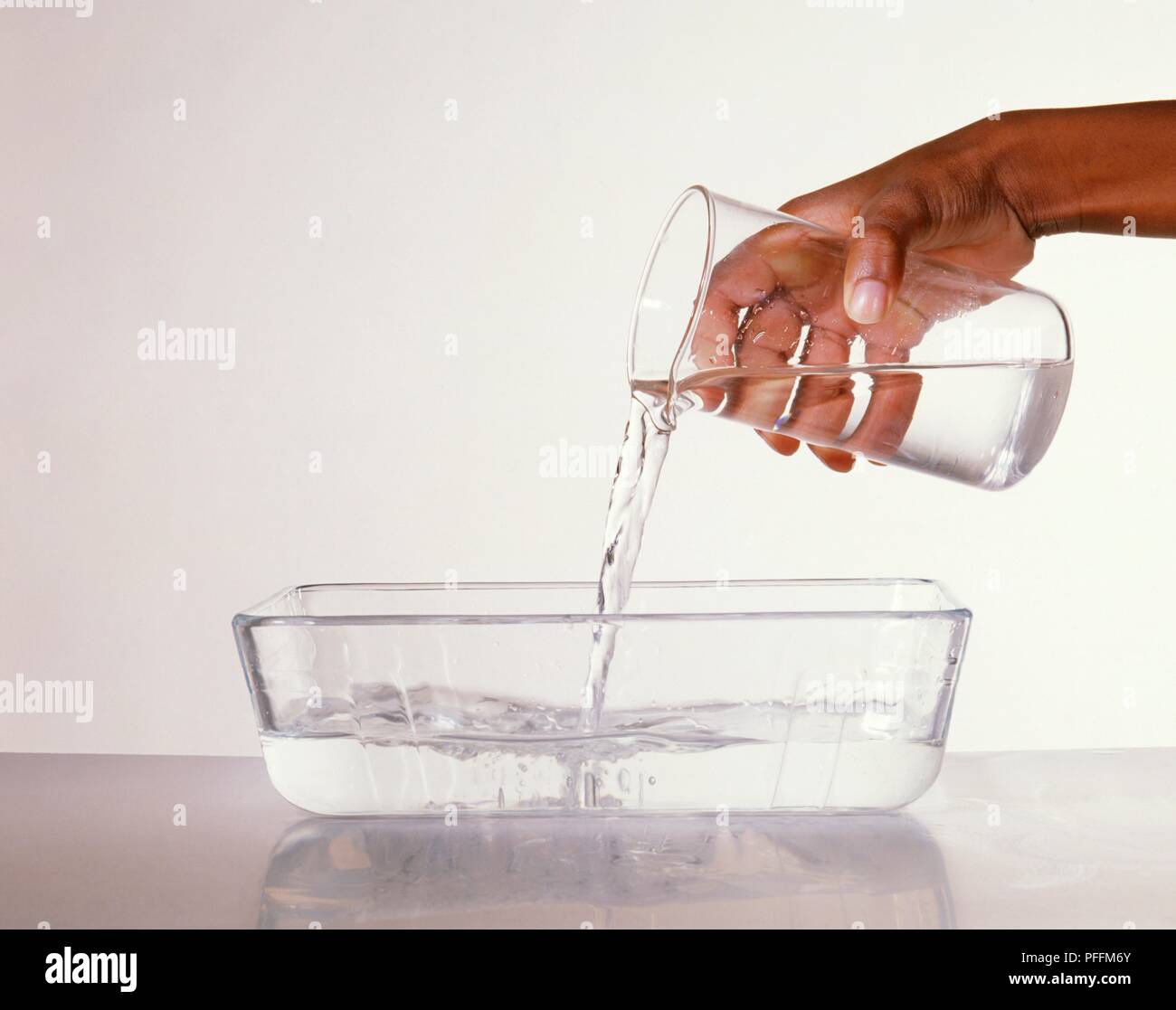 Boy's hand pouring water from a beaker into a glass dish, closeup