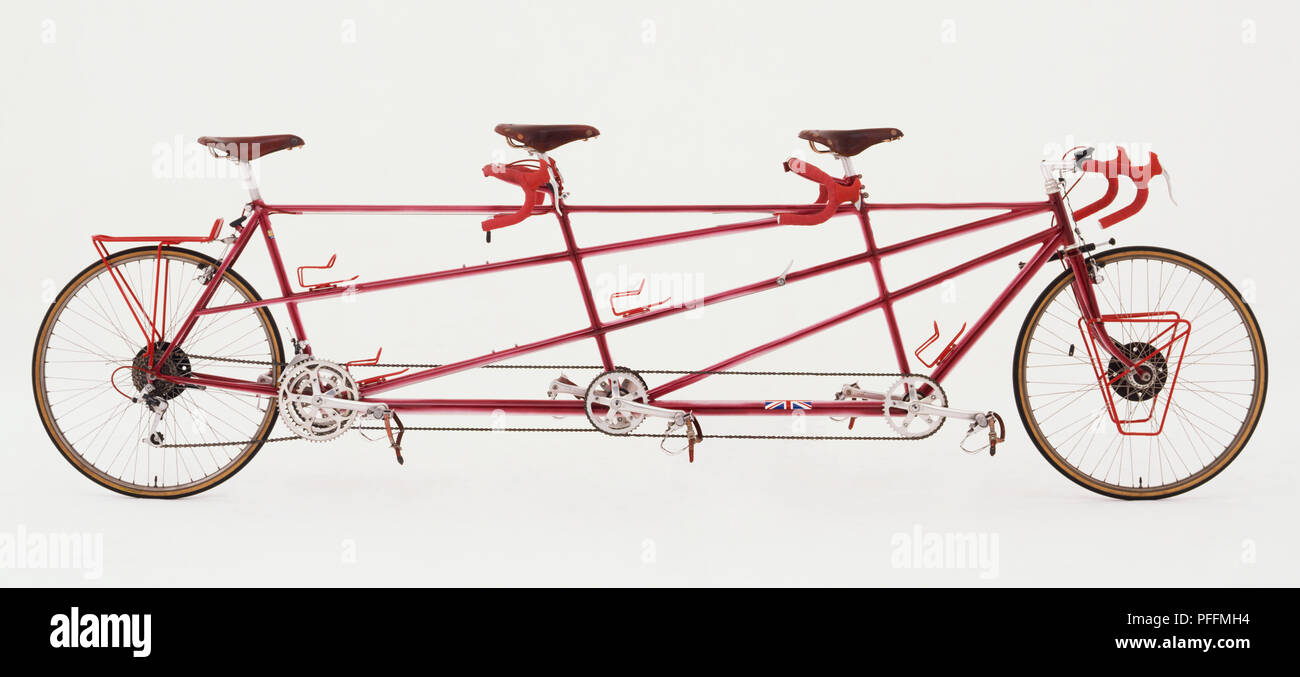 Side View Of A Red, Three Seater Triple Tandem Bicycle. With Three Seats And Three Sets Of Handle Bars. Stock Photo