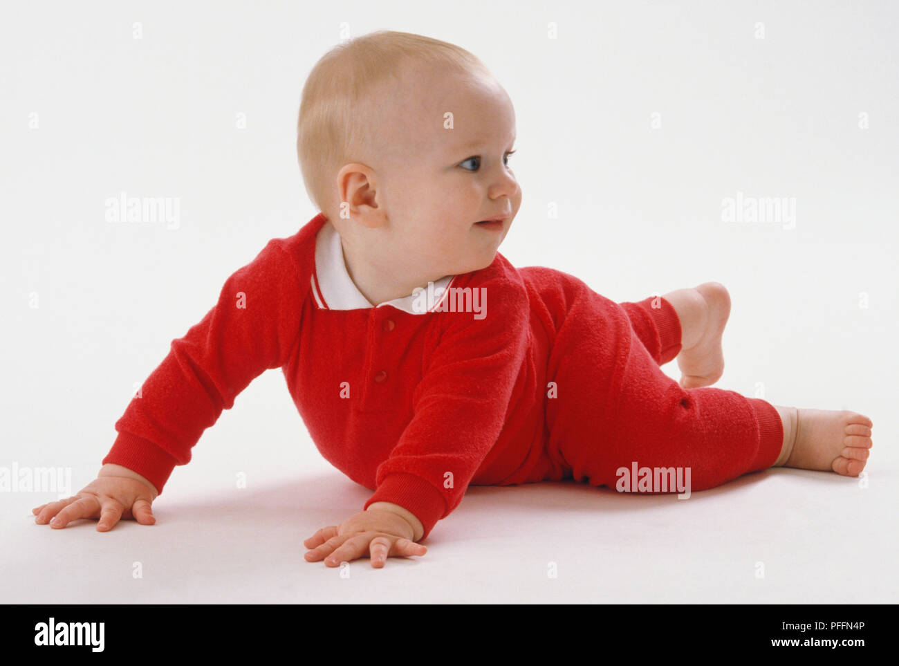 Baby wearing red jumpsuit lying on his front raising himself on his arms looking over his shoulder Stock Photo Alamy