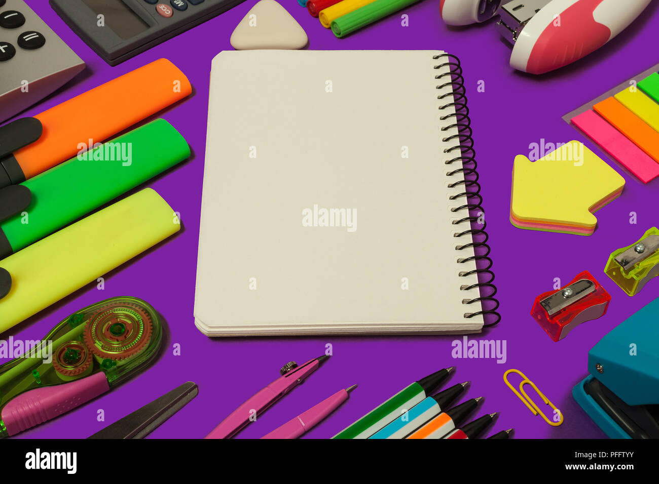 various stationary surrounding an opened notebook lying on a purple background. concept of office and educational chancery Stock Photo