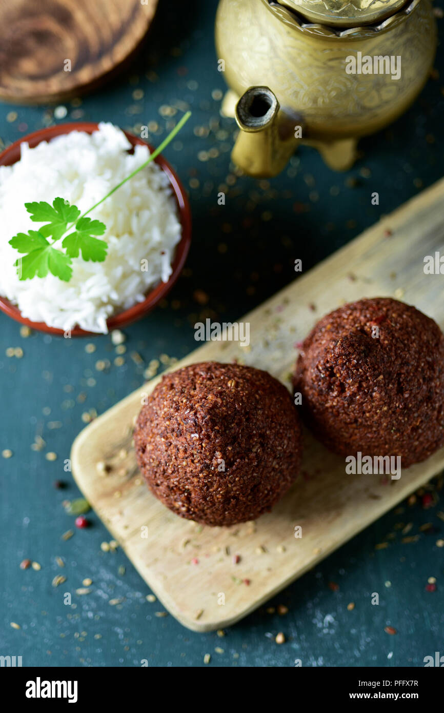 high angle view of some kibbeh, a levantine dish, an earthenware bowl with rice and a golden teapot on a rustic wooden table Stock Photo