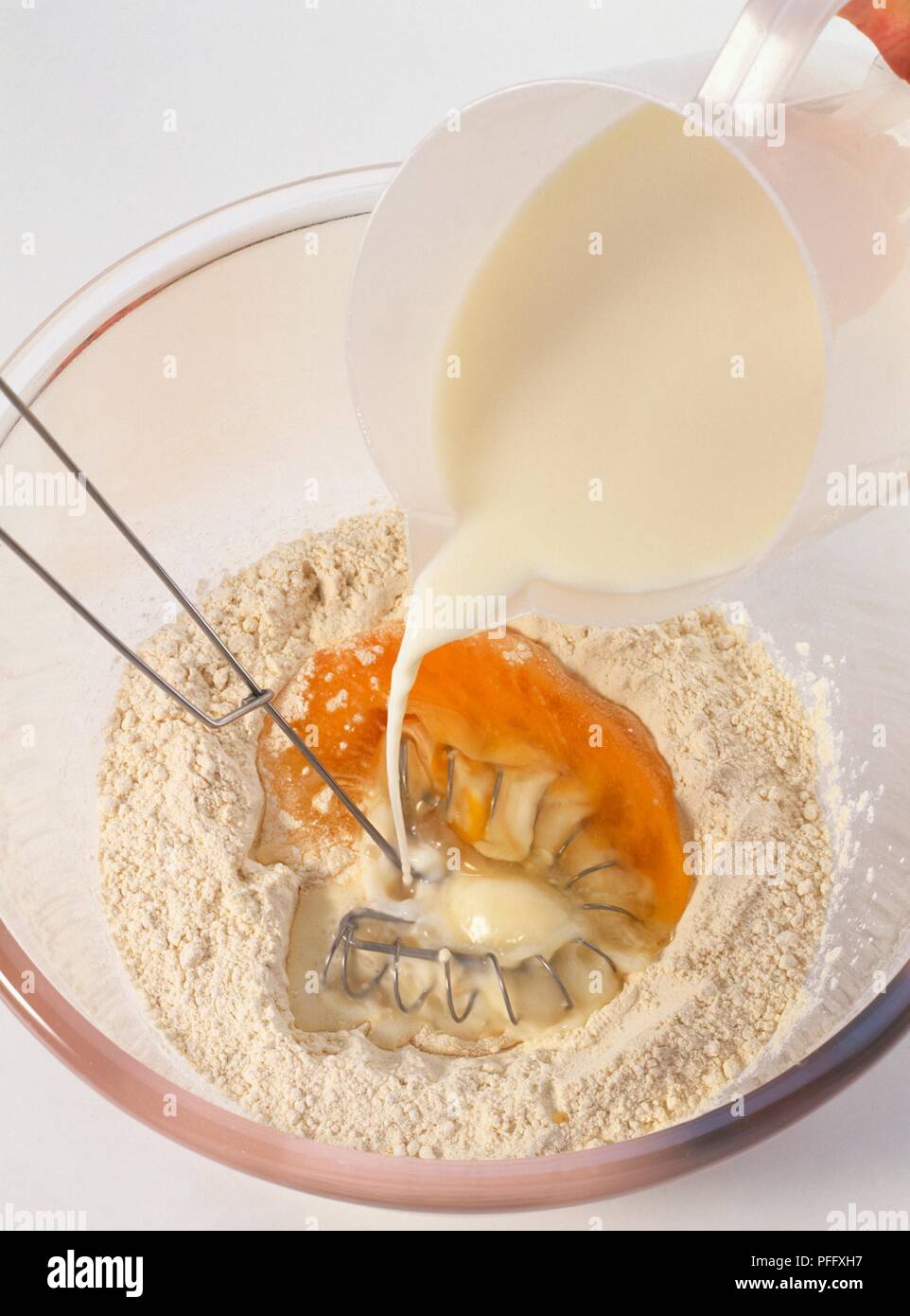 Making pancake batter, pouring milk onto eggs and flour in bowl Stock