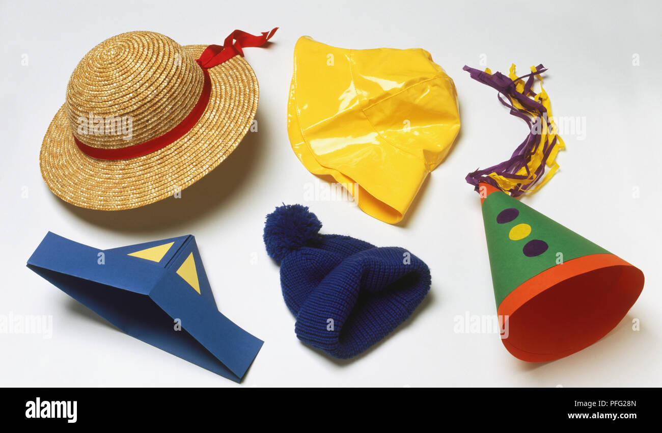 Five different hats, including straw hat, yellow rain hat, blue paper hat, blue wooly bobble hat and cone-shaped green and red paper hat with blue and yellow dots Stock Photo