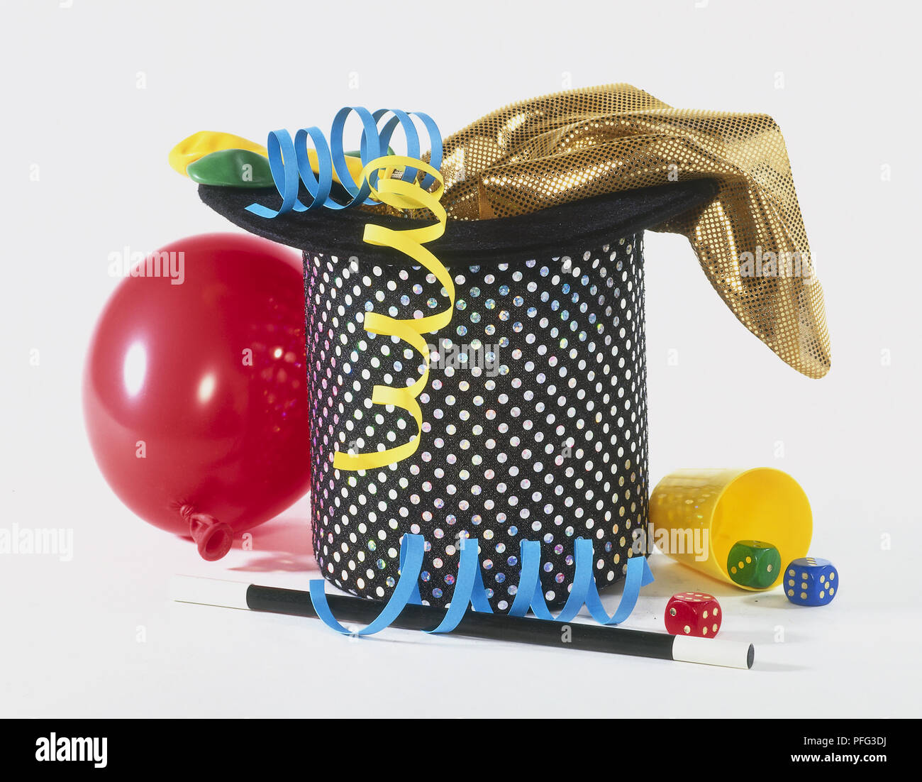 Black sequinned top hat, gold cloth, red balloon, magic wand, three dice and blue and yellow streamers Stock Photo