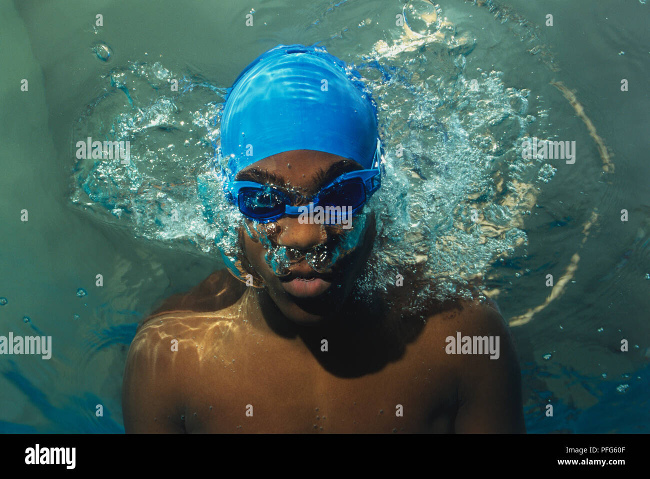 Boy underwater wearing blue goggles and blue swim cap, breathing out