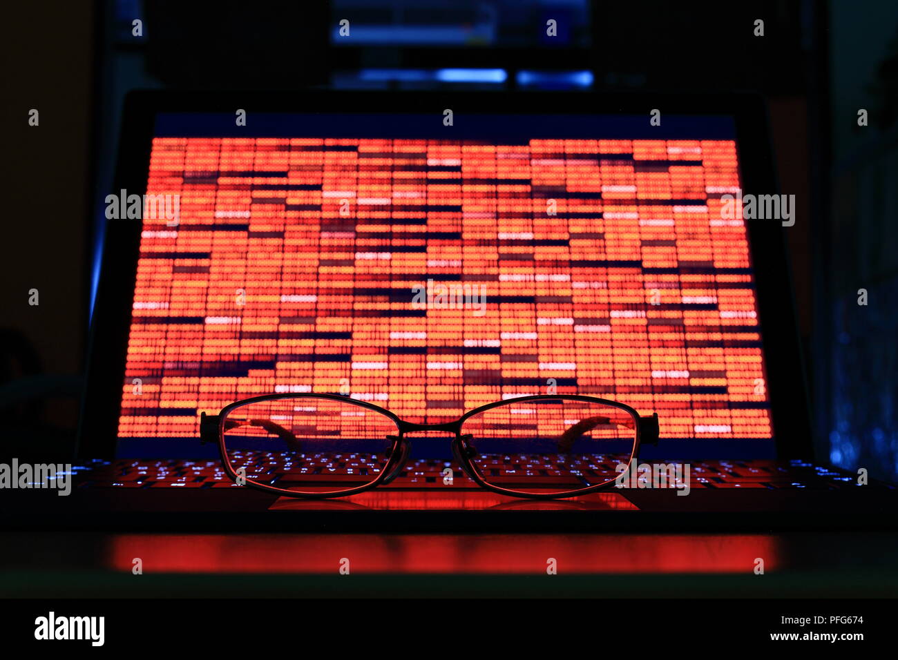 Data crisis and computer crime. glasses in front of computer notebook with red binary code in a dark room. technology, binary data, computer crime Stock Photo